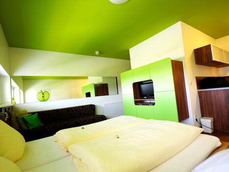 Ein Zimmer mit grüner Decke, schwarzem Sofa und Küche. | © Hotel Greenrooms