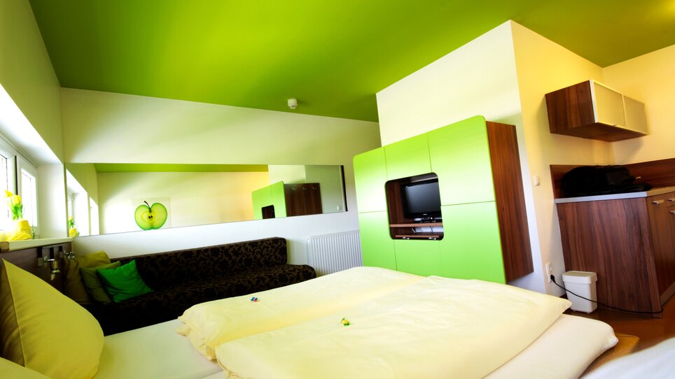 Ein Zimmer mit grüner Decke, schwarzem Sofa und Küche. | © Hotel Greenrooms