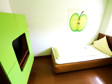 Ein Zimmer mit einem grünen Schrank, einem Bett und einem Apfelbild an der Wand. | © Hotel Greenrooms