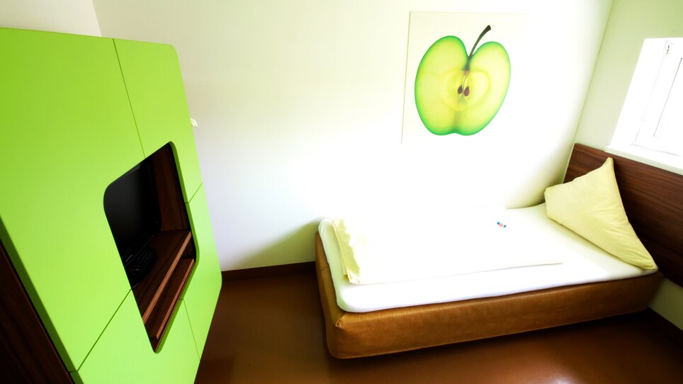 Ein Zimmer mit einem grünen Schrank, einem Bett und einem Apfelbild an der Wand. | © Hotel Greenrooms