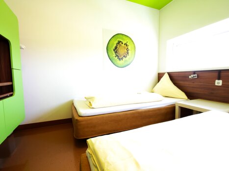 Ein Zimmer mit zwei Betten, grünem Farbdesign und Kiwi-Bild. | © Hotel Greenrooms