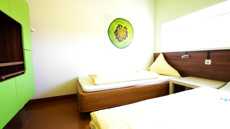 Ein Zimmer mit zwei Betten, grünem Farbdesign und Kiwi-Bild. | © Hotel Greenrooms