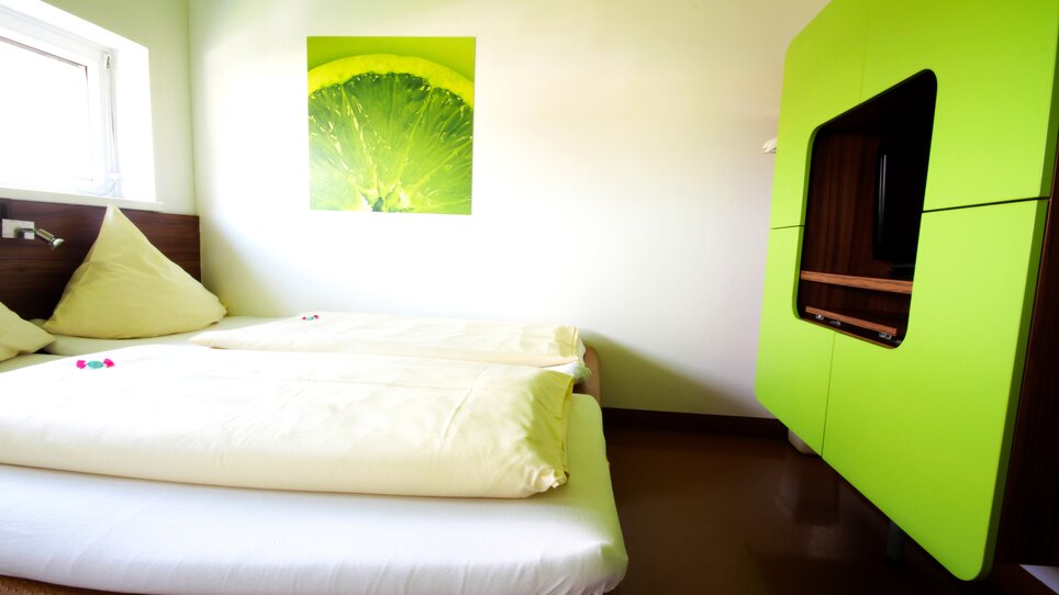 Ein helles Schlafzimmer mit zwei Betten und einem grünen Schrank.