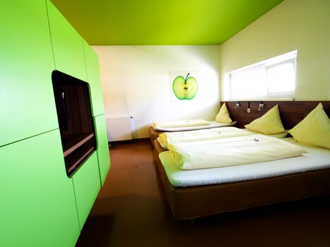 Ein Zimmer mit grüner Einrichtung und drei Betten, dekoriert mit einem Apfelbild.