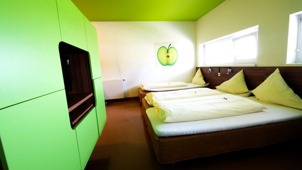 Ein Zimmer mit grüner Einrichtung und drei Betten, dekoriert mit einem Apfelbild.