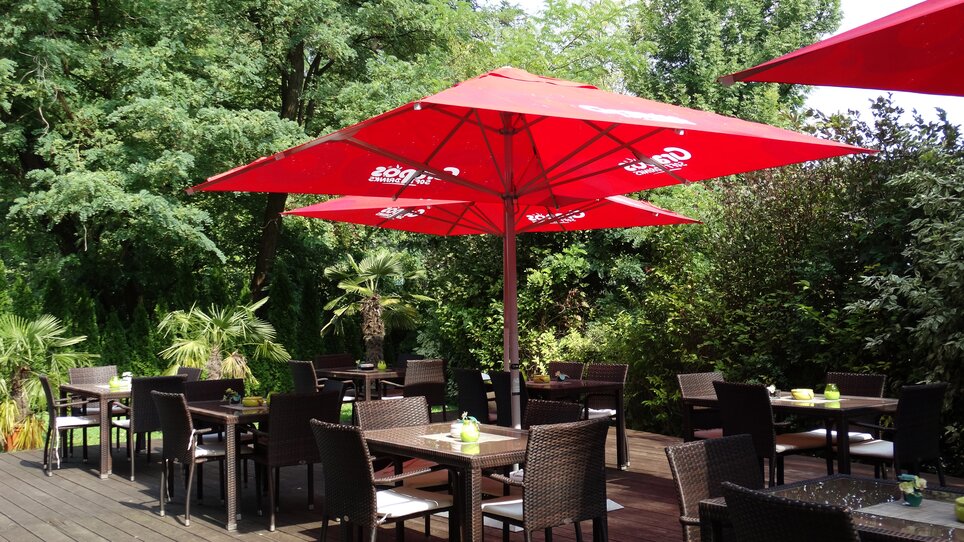 Terrasse mit roten Sonnenschirmen und Tischen im Freien.