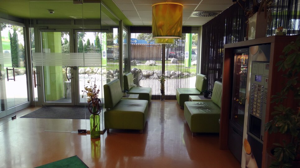Ein Empfangsbereich mit grünen Sitzmöbeln und einem Automaten.