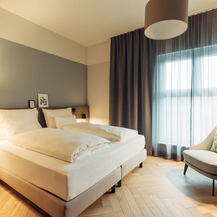 Helles Schlafzimmer mit zwei Betten und einem Sessel im harry's home Graz-Smart City. | © harry's home Graz-Smart City - Daniel Zangerl