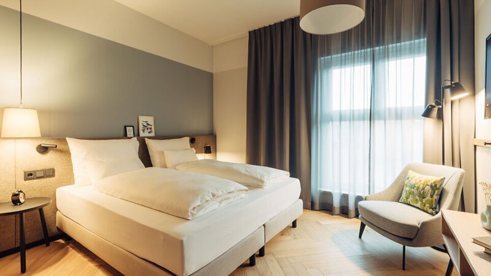 Helles Schlafzimmer mit zwei Betten und einem Sessel im harry's home Graz-Smart City. | © harry's home Graz-Smart City - Daniel Zangerl