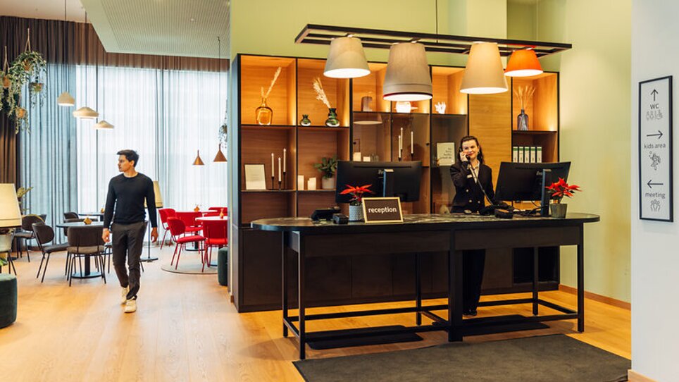 Eine helle Empfangsbereich mit einem Mitarbeiter am Telefon im harry's home Graz-Smart City. | © harry's home Graz-Smart City - Daniel Zangerl