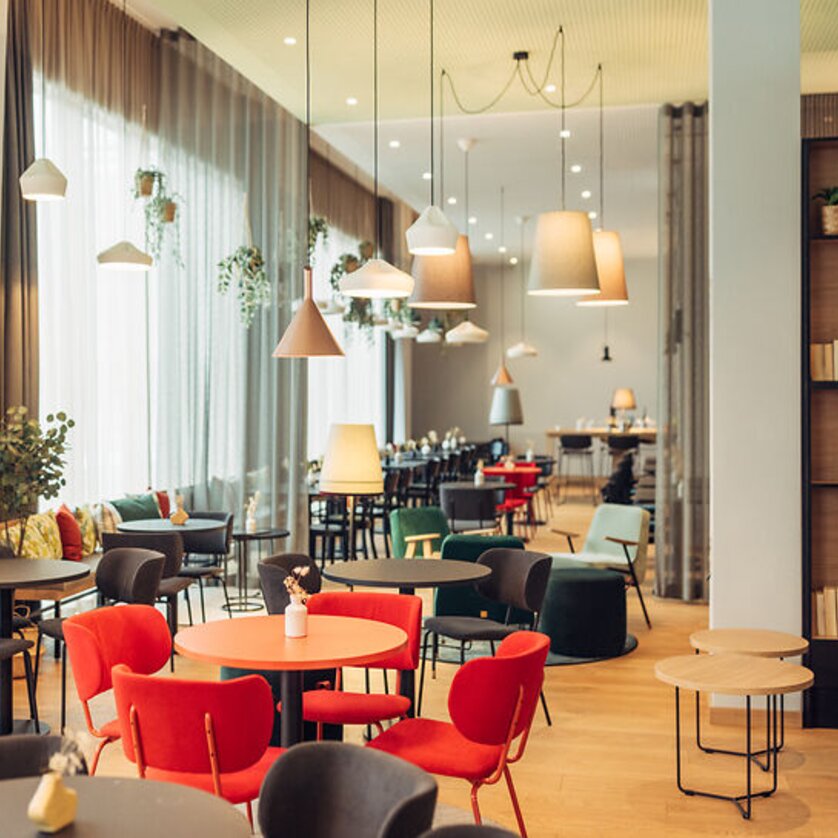 Hell erleuchtet Café mit bunten Stühlen und Pflanzen im harry's home Graz-Smart City. | © harry's home Graz-Smart City - Daniel Zangerl