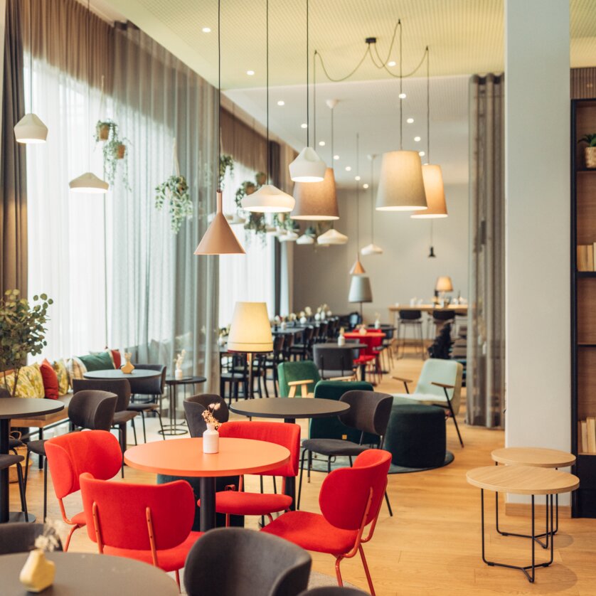 Brightly lit café with colorful chairs and plants at the harry's home Graz-Smart City. | © harry's home Graz-Smart City - Daniel Zangerl