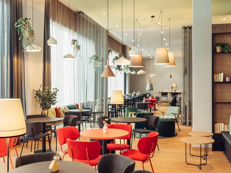 Brightly lit café with colorful chairs and plants at the harry's home Graz-Smart City. | © harry's home Graz-Smart City - Daniel Zangerl