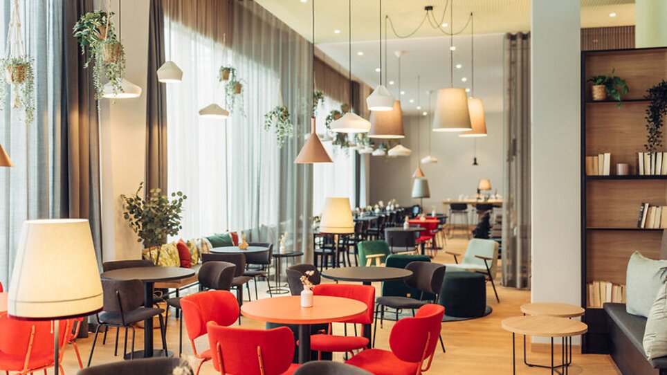 Hell erleuchtet Café mit bunten Stühlen und Pflanzen im harry's home Graz-Smart City. | © harry's home Graz-Smart City - Daniel Zangerl