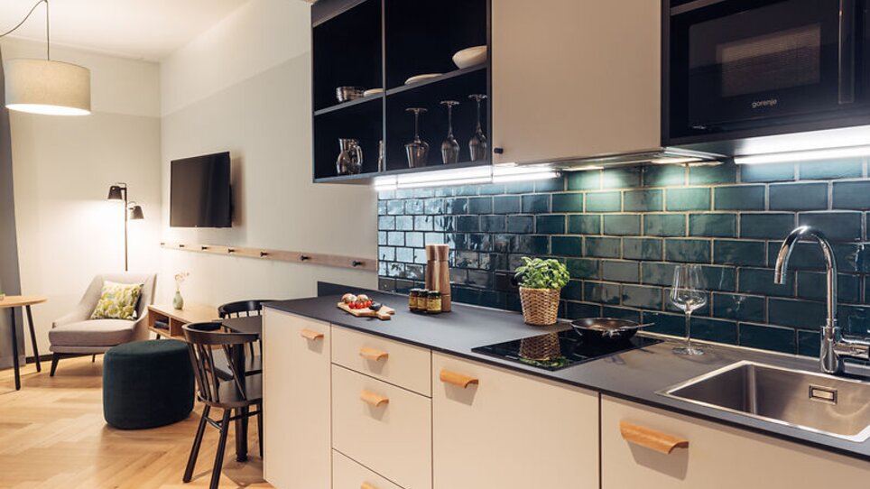 Küchenbereich mit Holzdetails, Essbereich und Wohnzimmer im harry's home Graz-Smart City. | © harry's home Graz-Smart City - Daniel Zangerl