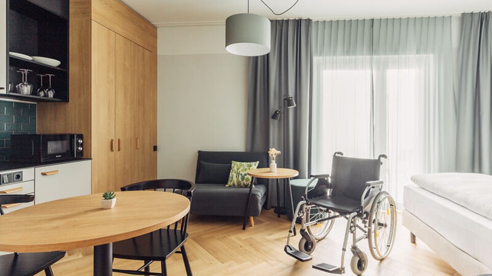 Innenansicht eines barrierefreien Zimmers mit einem Rollstuhl im harry's home Graz-Smart City. | © harry's home Graz-Smart City- Daniel Zangerl