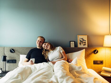 Liebespaar entspannend im Bett mit einer Tasse Kaffee im harry's home Graz-Smart City. | © harry's home Graz-Smart City - Daniel Zangerl