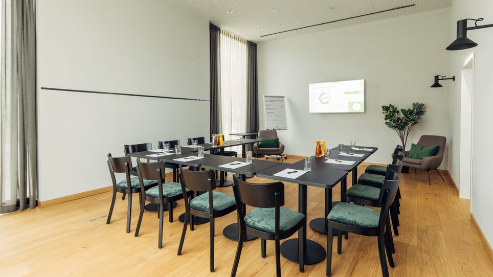A conference room with tables, chairs, and a screen at the harry's home Graz-Smart City. | © harry’s home hotels - Daniel Zangerl