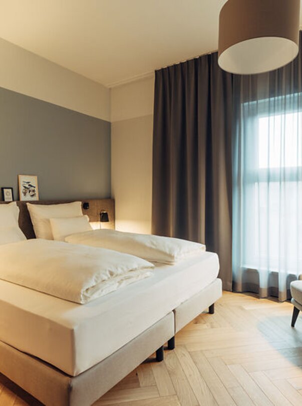Gemütliches Hotelzimmer mit Doppelbett und Lesesessel. | © Harrys Home Graz Smart City - Daniel Zangerl