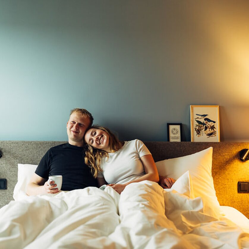 Harry's Home Graz Smart City | © Daniel Zangerl A couple sits in bed, happy and relaxed, surrounded by white blankets. | © Daniel Zangerl