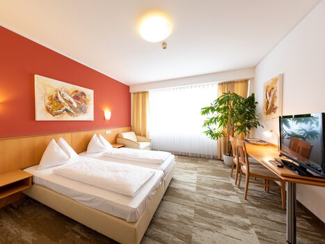 Modern room with two beds, TV, and plants. | © Harry Schiffer