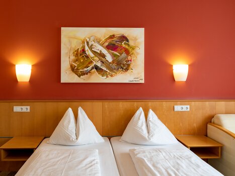 A bright room with two beds, red wall, and modern art. | © Harry Schiffer