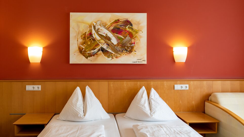 Ein helles Zimmer mit zwei Betten, roter Wand und moderner Kunst. | © Harry Schiffer