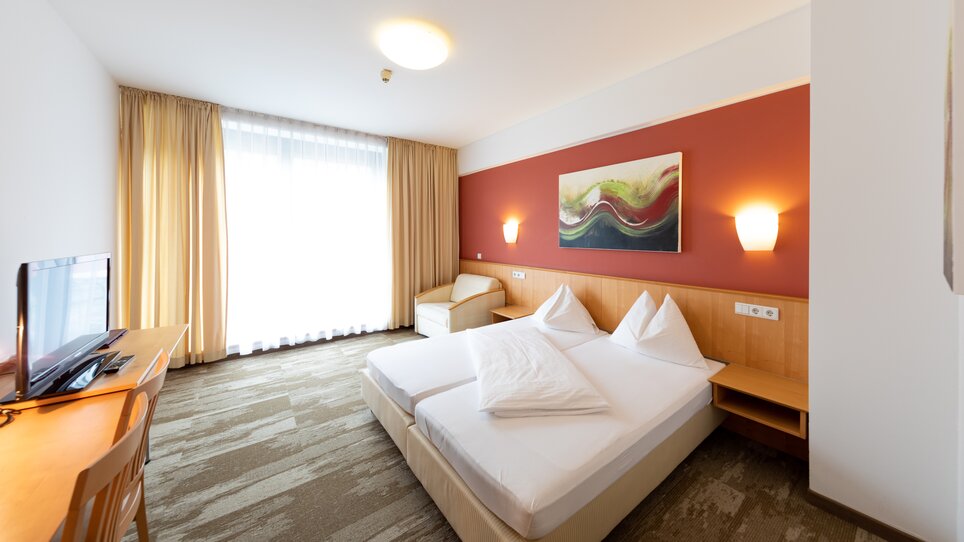 Helles Doppelzimmer mit zwei Betten und einem Fernseher. | © Harry Schiffer