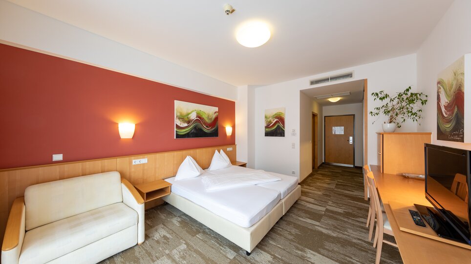 Helles Hotelzimmer mit Doppelbett, Couch und Schreibtisch. | © Harry Schiffer