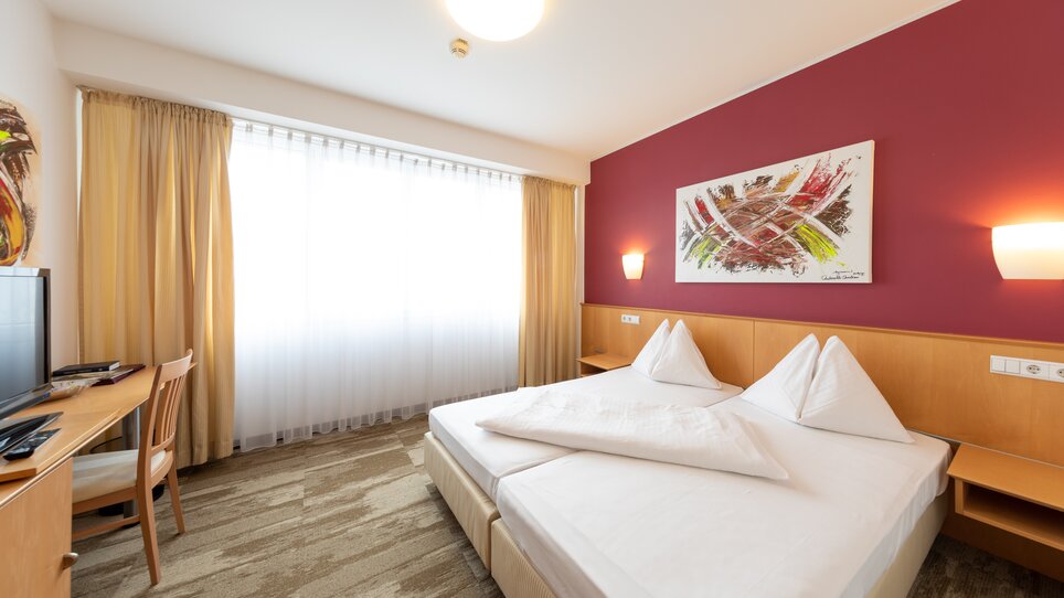 Hell eingerichtetes Zimmer mit Doppelbett und Fernseher. | © Harry Schiffer