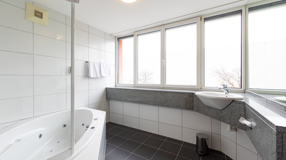 Helles Badezimmer mit Badewanne, Fenstern und modernen Armaturen. | © Harry Schiffer