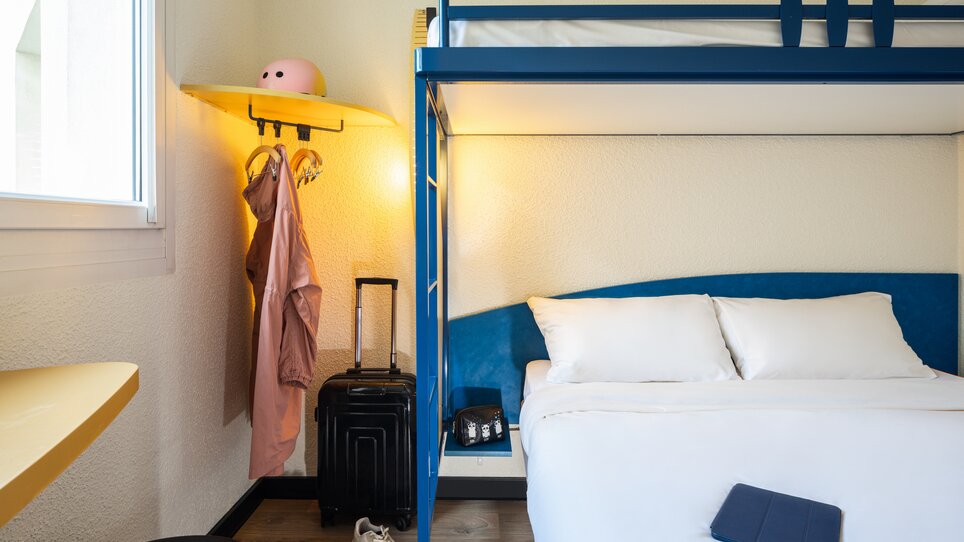Hell eingerichtetes Zimmer mit Doppelbett, einem Hochbett, Koffer und Kleidung. | © Ibis Budget