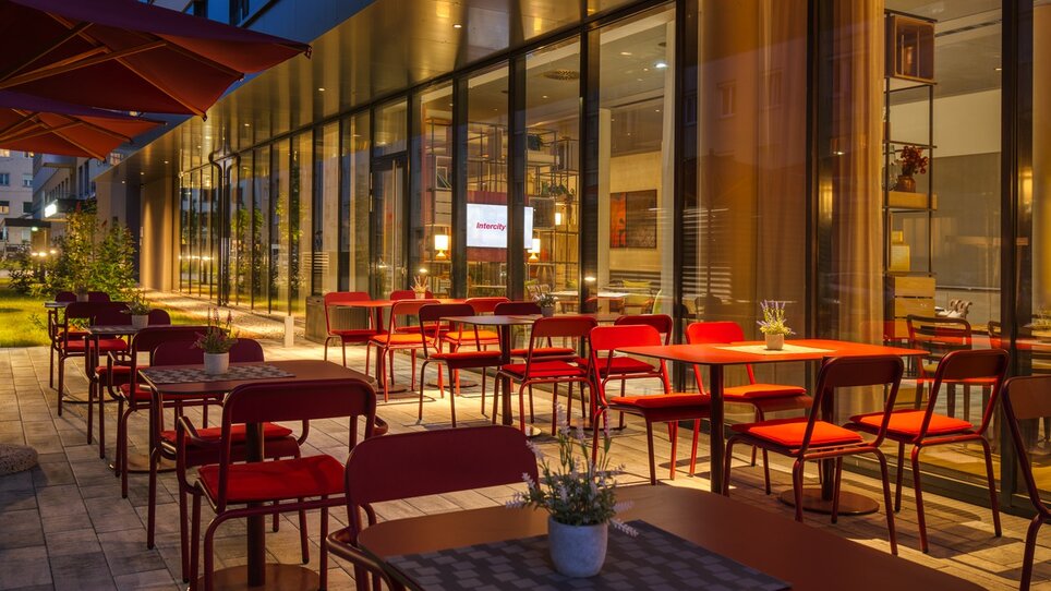 Gemütlicher Außenbereich des IntercityHotel Graz mit roten Stühlen und Tischen. | © ICHG