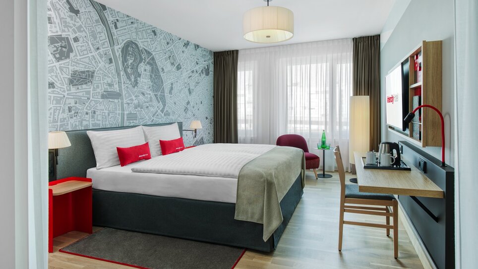 Helles Hotelzimmer mit Doppelbett, Schreibtisch und Kartendekor. | © ICHG