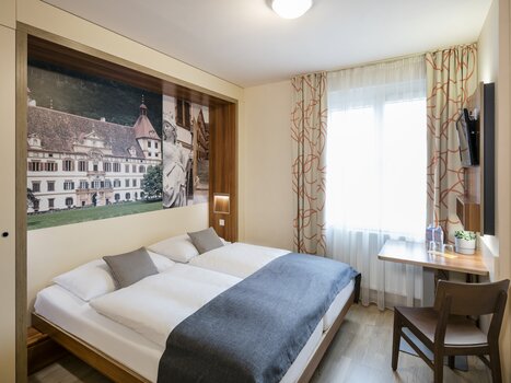 Modern hotel room with double bed, desk, and window. | © JUFA Hotel Graz City