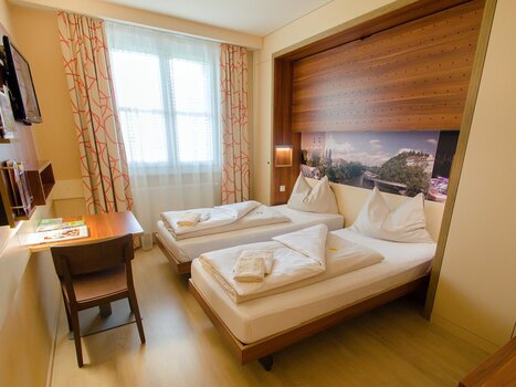 Cozy hotel room featuring two single beds and a desk. | © JUFA Hotel Graz City
