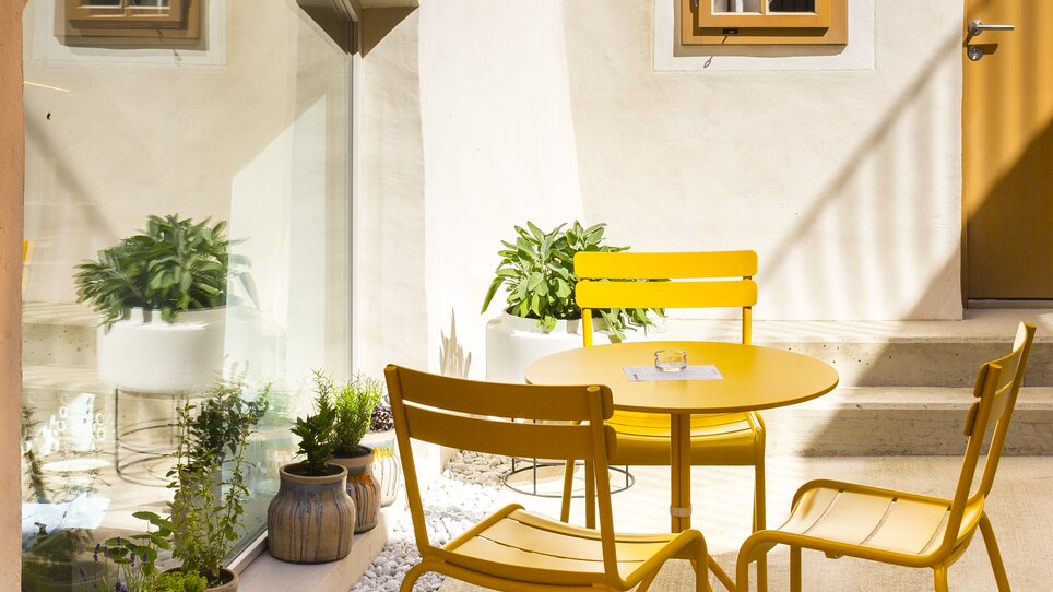 Ein gelber Tisch mit Stühlen im Innenhof des Hotel KAI 36. | © KAI 36