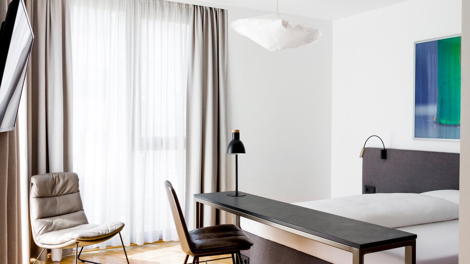 Helles Zimmer mit großem Bett, Tisch, Stuhl und eleganter Lampe. | © Lendhotel