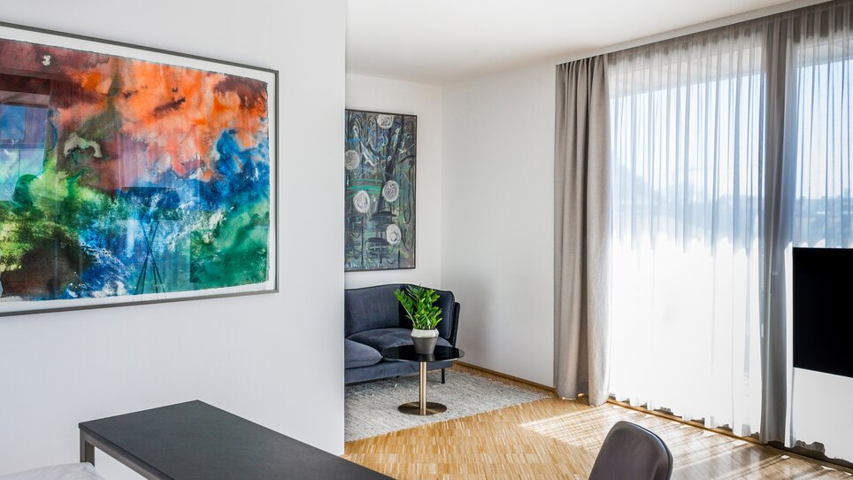 Modernes Zimmer mit Kunstwerk, gemütlicher Sitzecke und großen Fenstern. | © Lendhotel