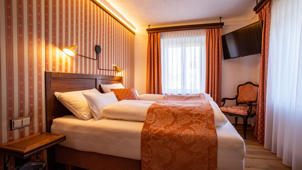 Ein Hotelzimmer mit Doppelbett, orangefarbenen Akzenten und TV. | © Lendplatzl GmbH