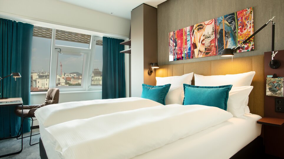 Modernes Zimmer mit Doppelbett, Kunstwerk und Blick auf Graz. | © Motel One Austria GmbH