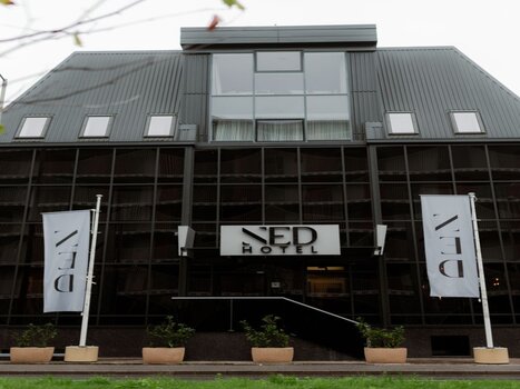 Das NED Hotel in Graz mit Spiegelglasfassade und Hotelbanner. | © NED Hotel