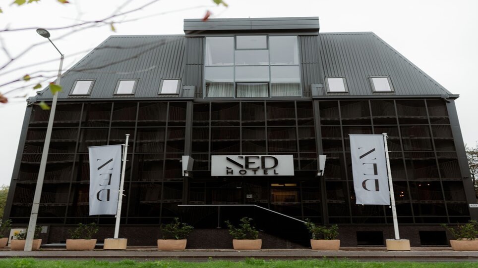 Das NED Hotel in Graz mit Spiegelglasfassade und Hotelbanner. | © NED Hotel