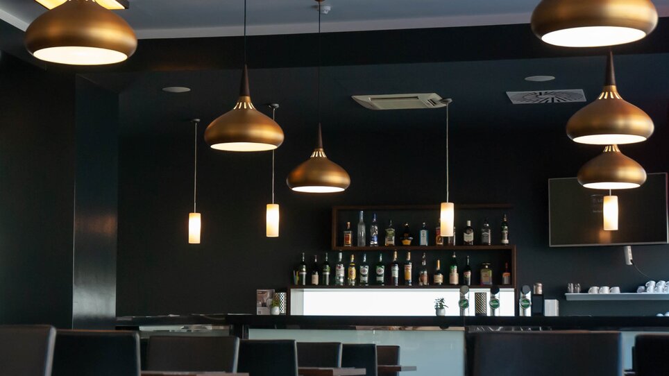 Innenraum eines Restaurants mit hängenden Lampen und einer Bar im Hintergrund. | © PLAZA INN Graz City