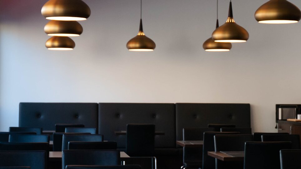 Ein Innenraum mit eleganten Hängelampen und schwarzen Stühlen. | © PLAZA INN Graz City