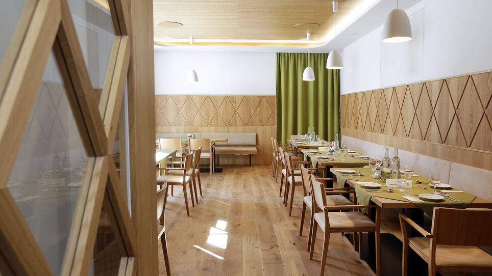 Una vista di un ristorante con mobili in legno e coperture verdi. | © Foto Pachernegg