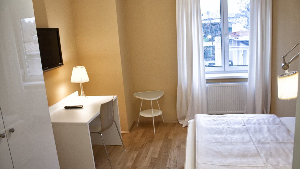 Modern bedroom featuring a desk, TV, and window view. | © Rueckert