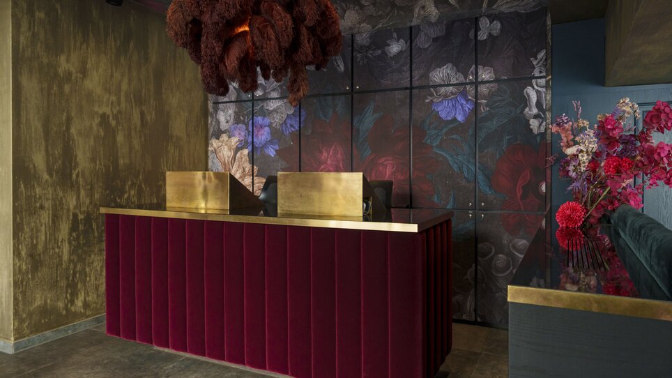 Receptione moderna con velluto rosso, accenti dorati e motivi floreali. | © Aiola Living