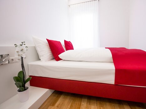 Stanza luminosa con letto matrimoniale e cuscini rossi. | © sHome Hotel