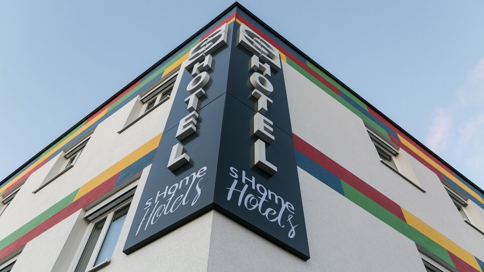 Facciata dell'hotel sHome con strisce colorate e grande insegno. | © sHome Hotel